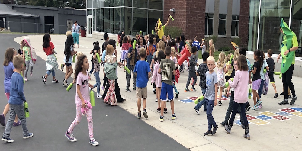 a large group of students on the playground playing with adults dressed as fruits and vegetables