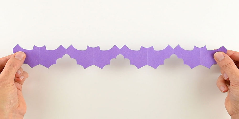 two hands holding a cutout of purple paper bats