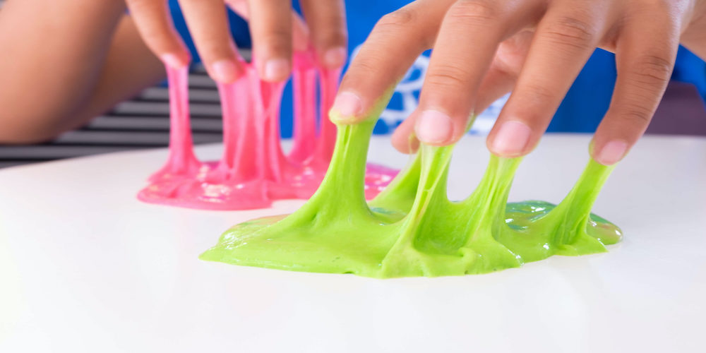 fingers attached to a green and pink slime mixture on a white surface